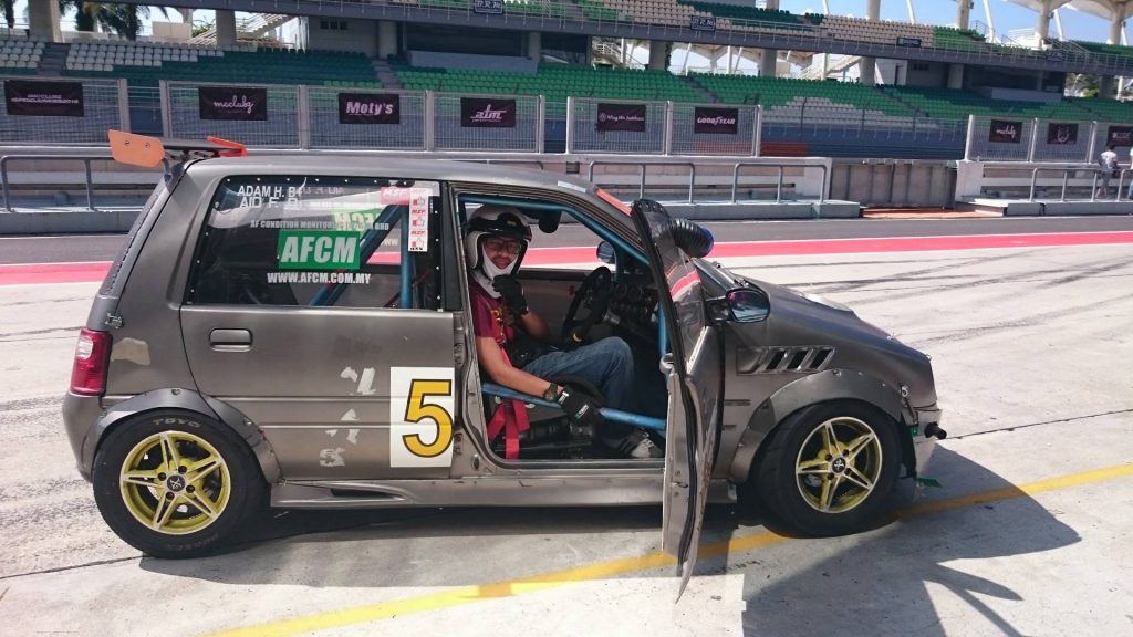 Dr Aid Fawzal wearing a helmet sitting in a modified car at a racetrack pit lane